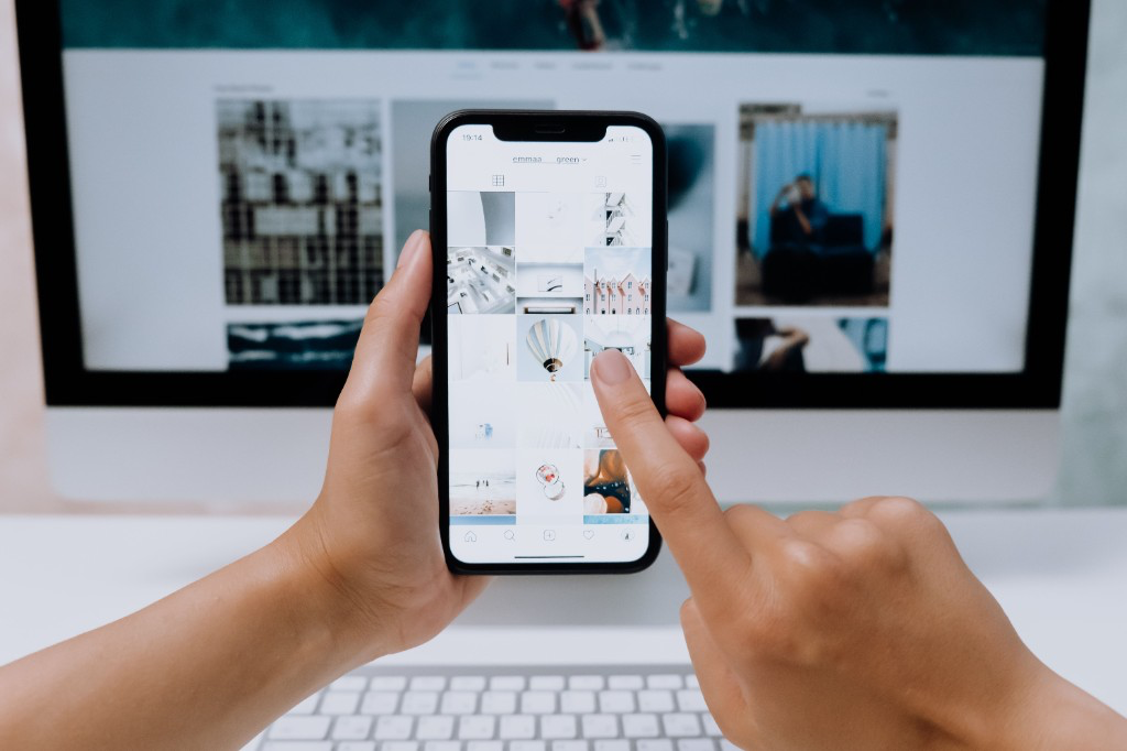 The Scroll Is Dead article cover: hands holding a smartphone showing a vertical photo feed, with a desktop screen in the background